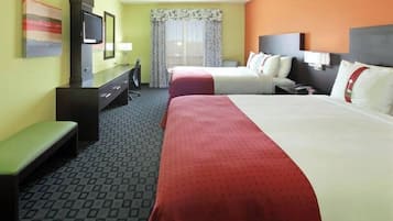 A hotel room with two beds, a desk with a television, a bench, and a window with curtains.
