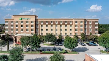 A Holiday Inn hotel with a brick facade, multiple floors, and a parking lot with several cars.
