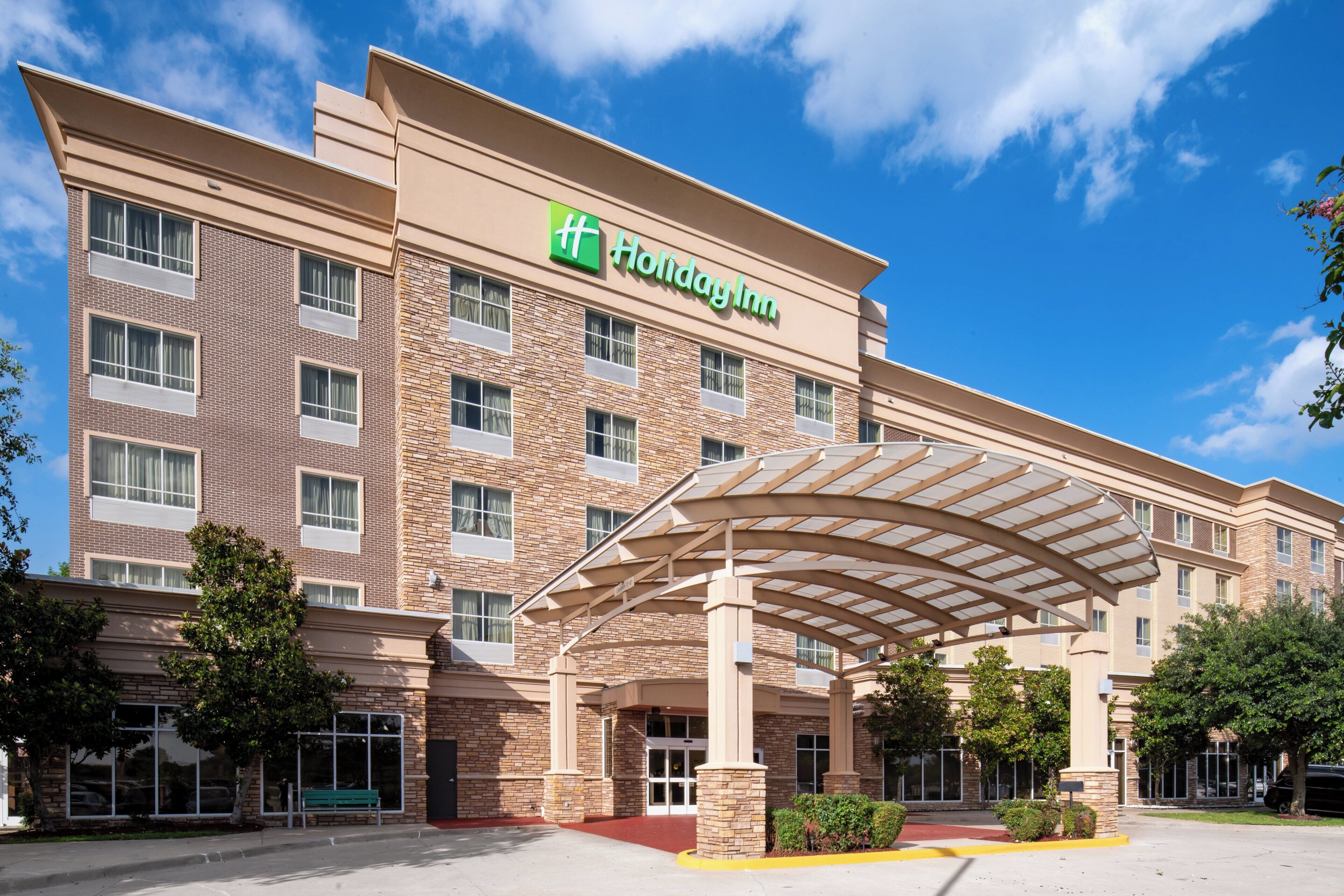 A Holiday Inn hotel with a brick facade, large windows, and a covered entrance.