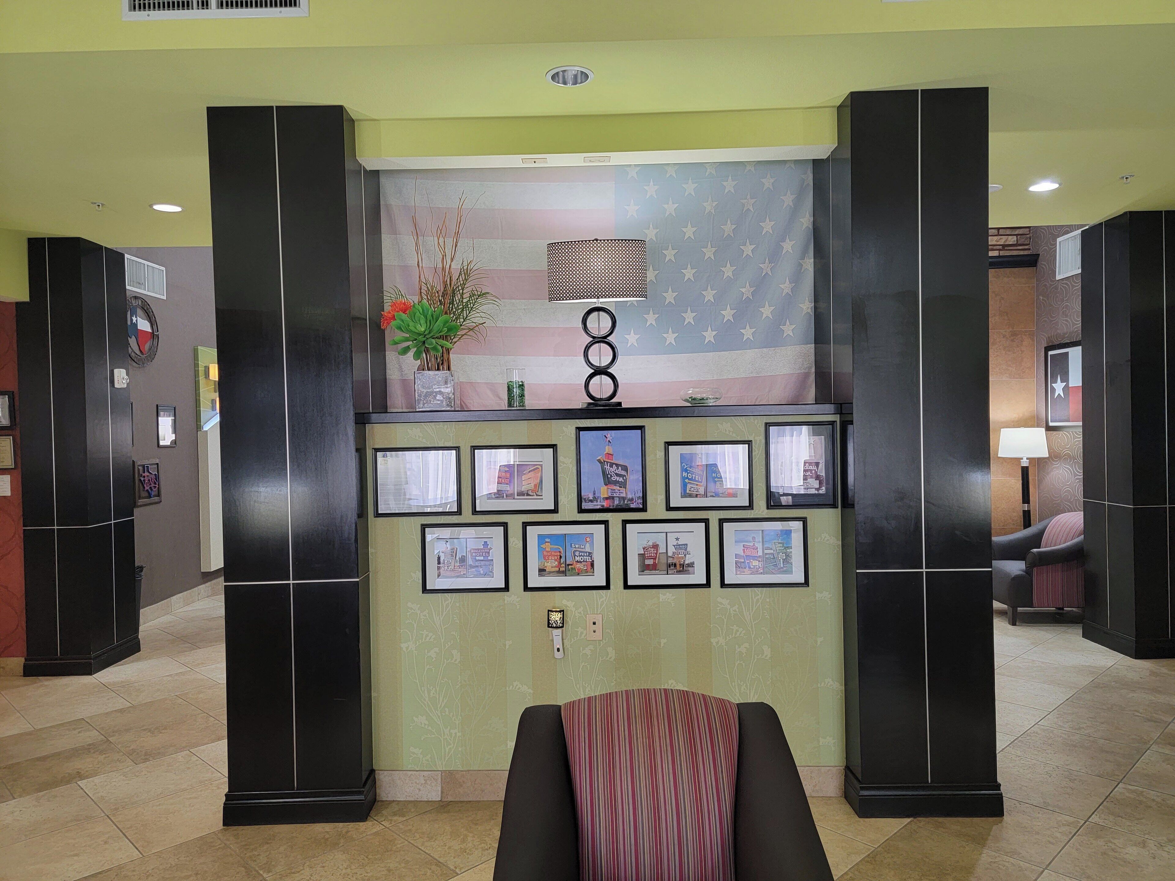 A reception area with a wall decorated with framed pictures, a plant, and a lamp.