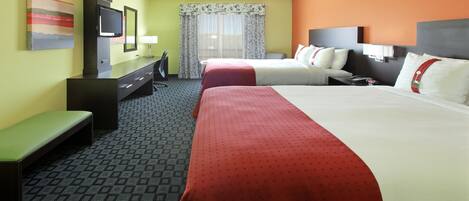 A hotel room with two beds, a desk, a chair, a TV, and a window with curtains.