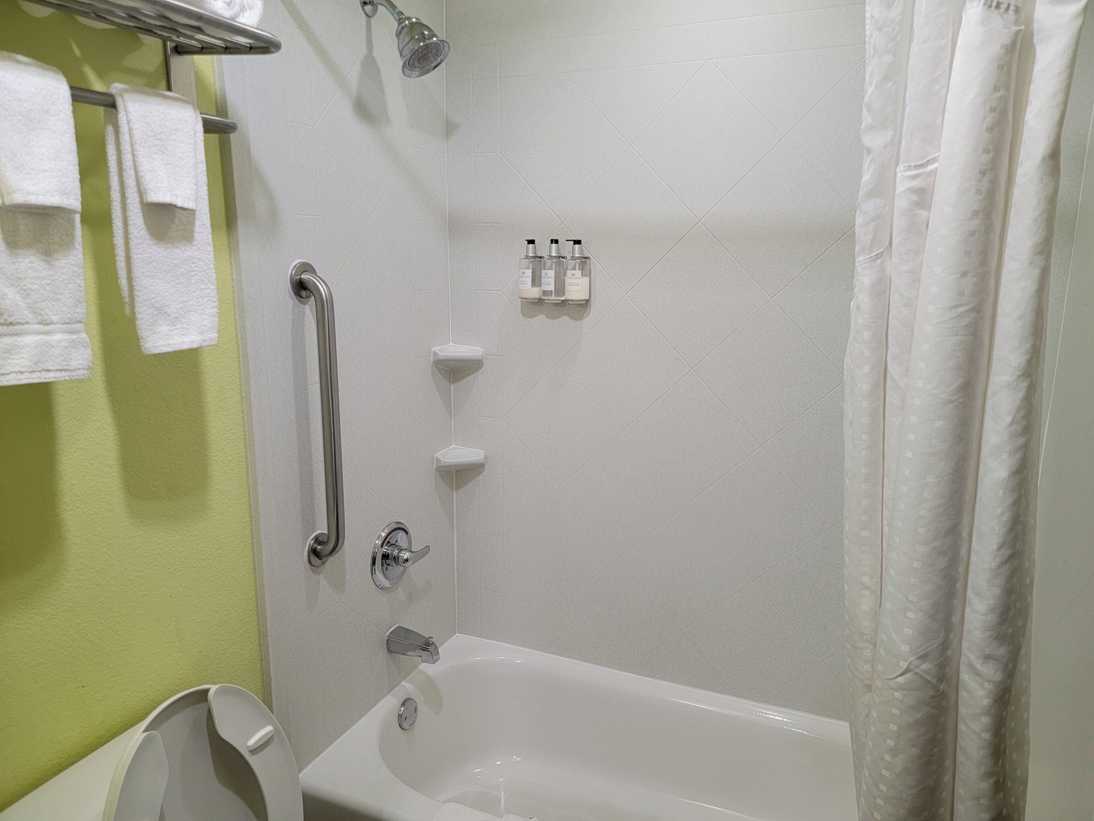 A bathroom with a bathtub, a shower, and a handrail.