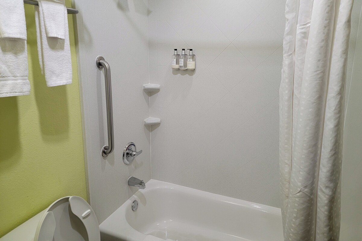 A bathroom with a bathtub, a shower, and a handrail.