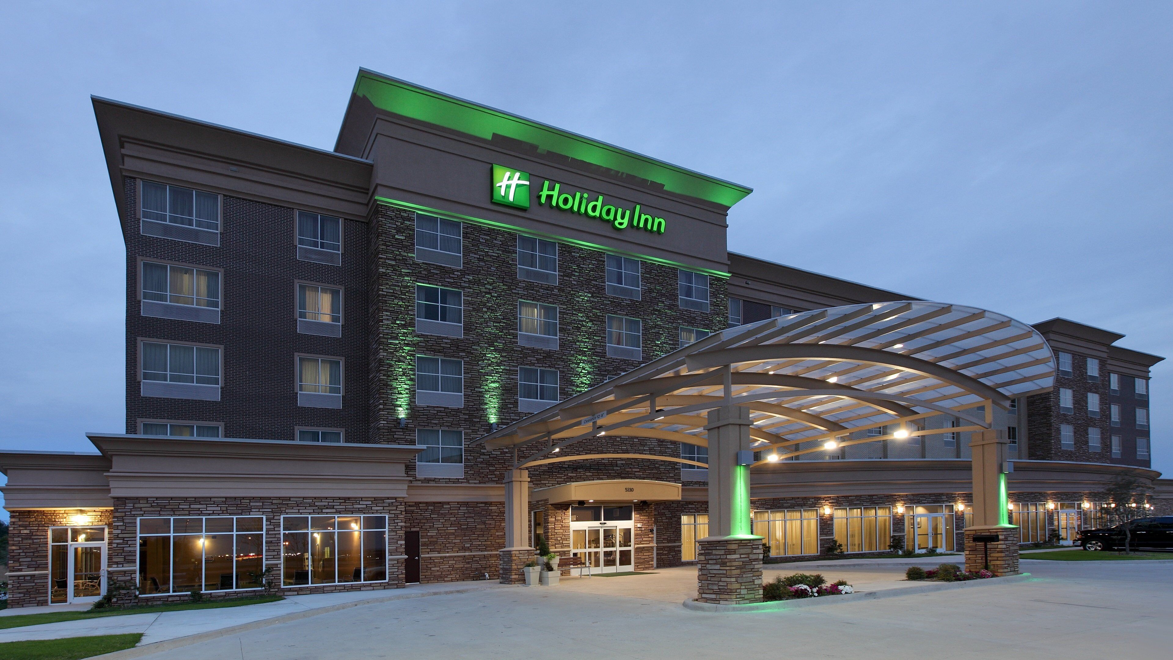 Un hôtel Holiday Inn avec une façade en briques, une entrée couverte et un éclairage extérieur soigné.