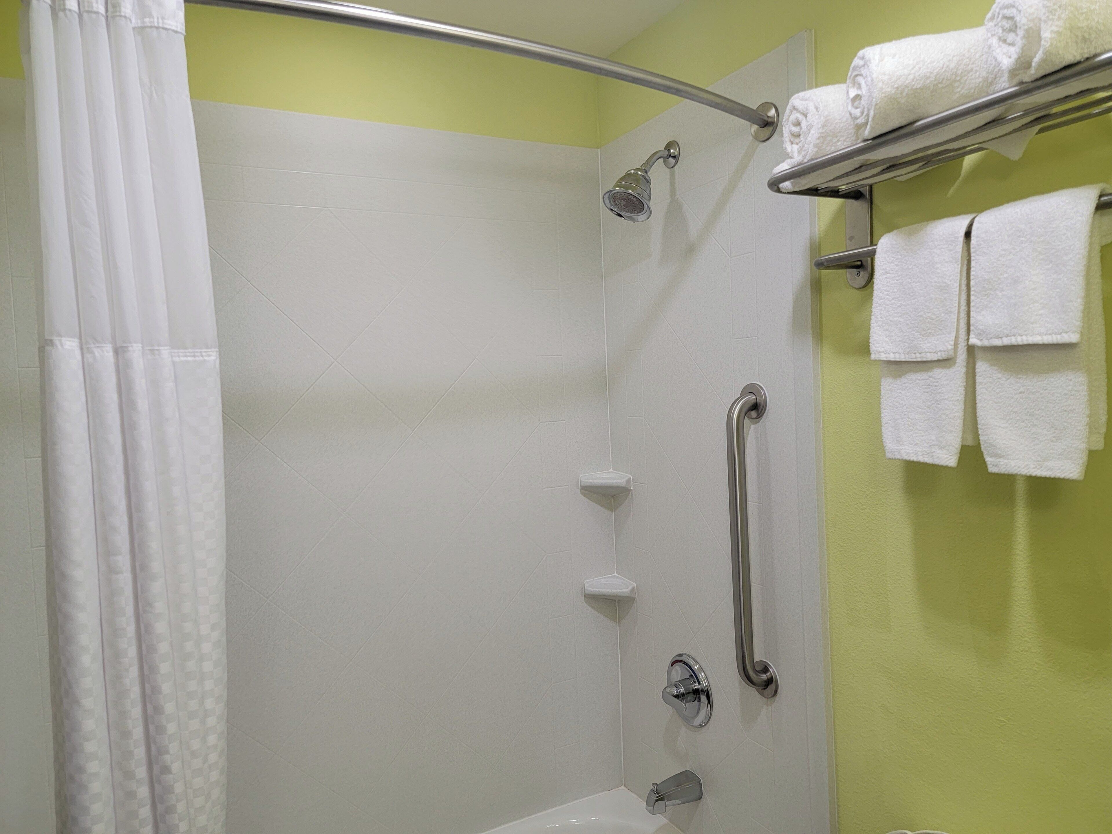 A shower area with a handrail, a showerhead, and a towel rack with towels.