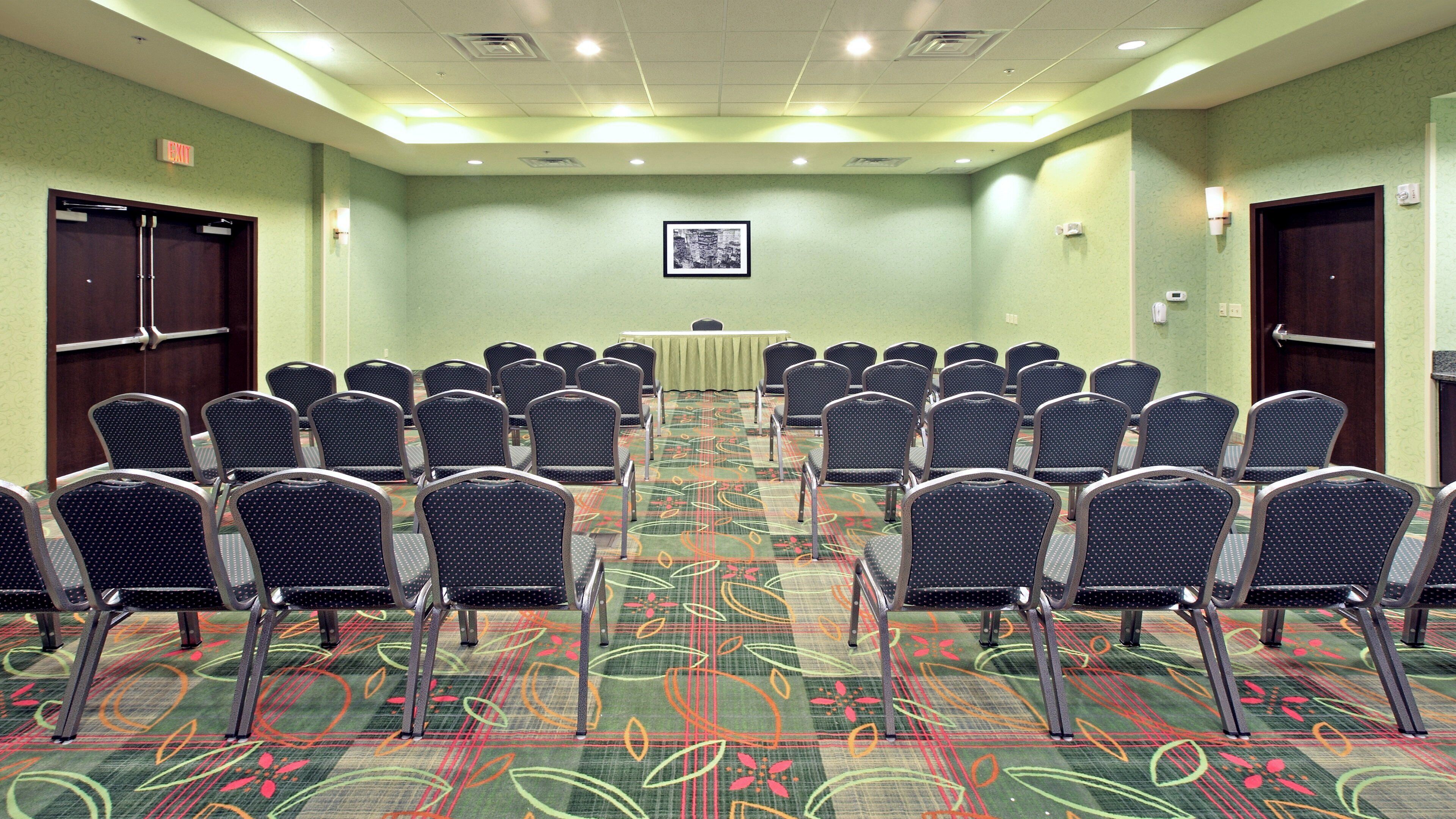 A conference room with rows of chairs, a table, and a patterned carpet.