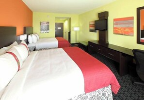 Une chambre d’hôtel avec deux lits, un bureau, une chaise, une télévision et des œuvres d’art accrochées aux murs.