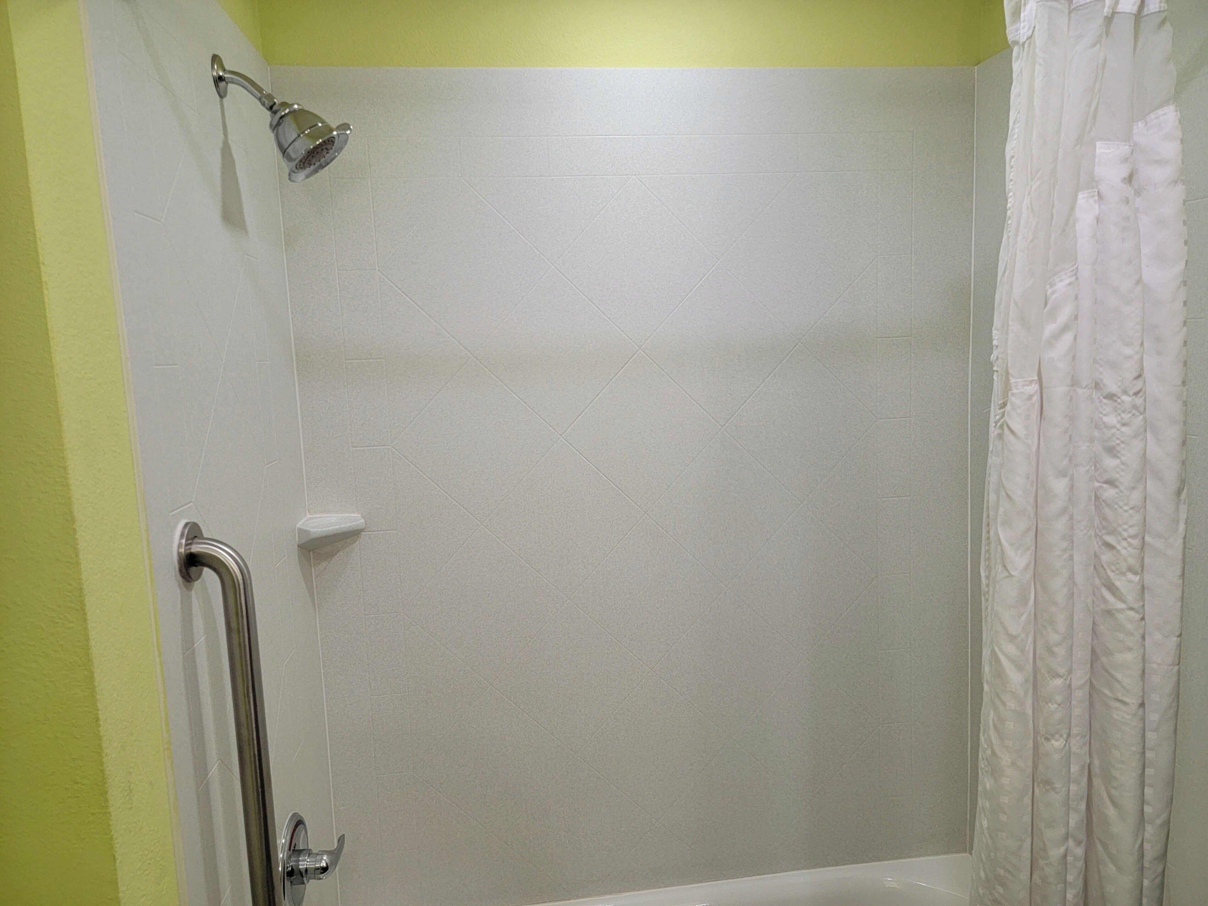 A shower area with a handheld showerhead, a grab bar, and a white shower curtain.
