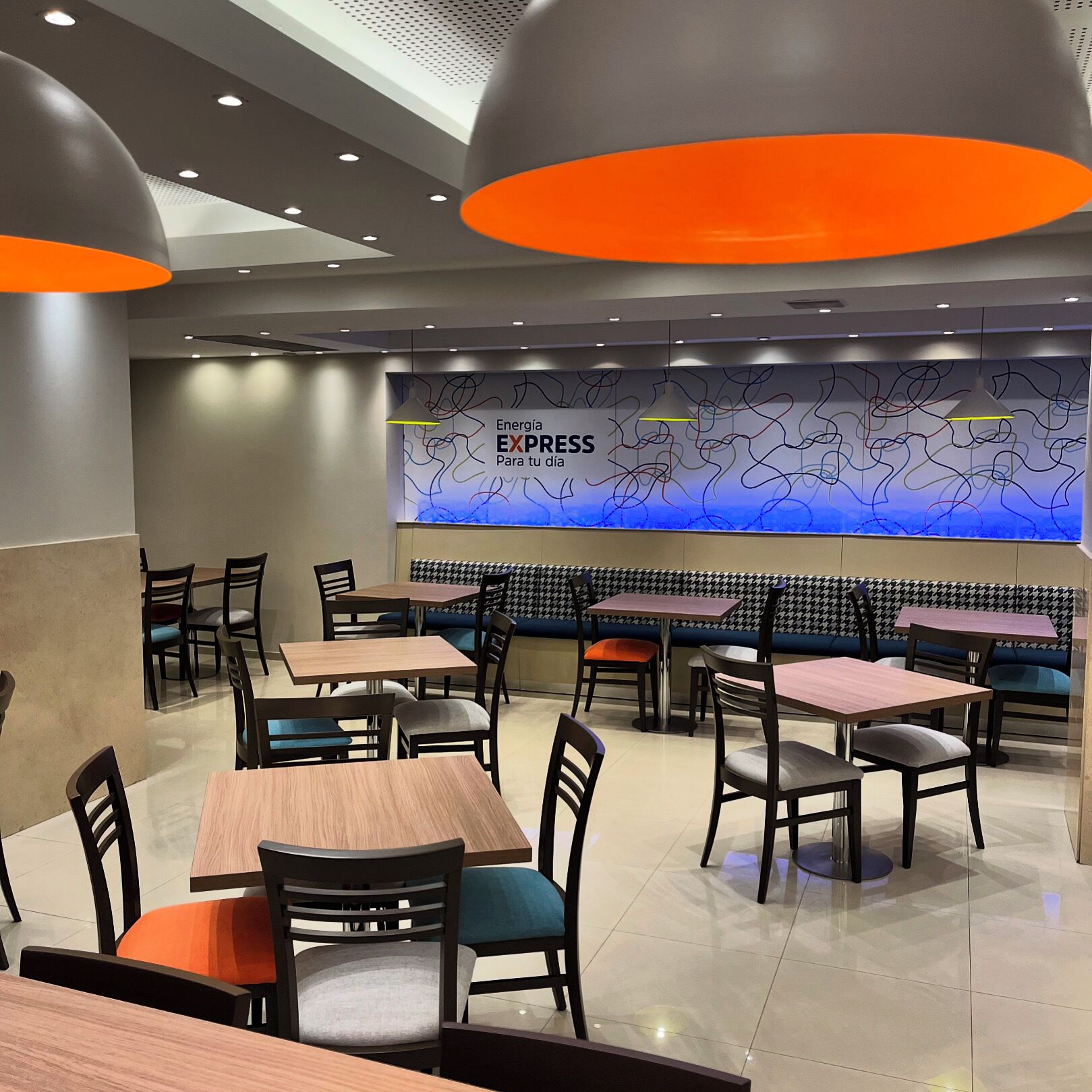 Interior de un restaurante con mesas y sillas, una pared con arte abstracto y un letrero que dice "Energía EXPRESS Para tu dia".