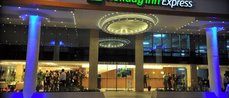 A Holiday Inn Express hotel entrance with a modern design, featuring a prominent sign, a glass facade, and a well-lit entrance area.
