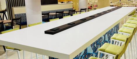 A modern cafeteria with a long white table and green cushioned chairs.