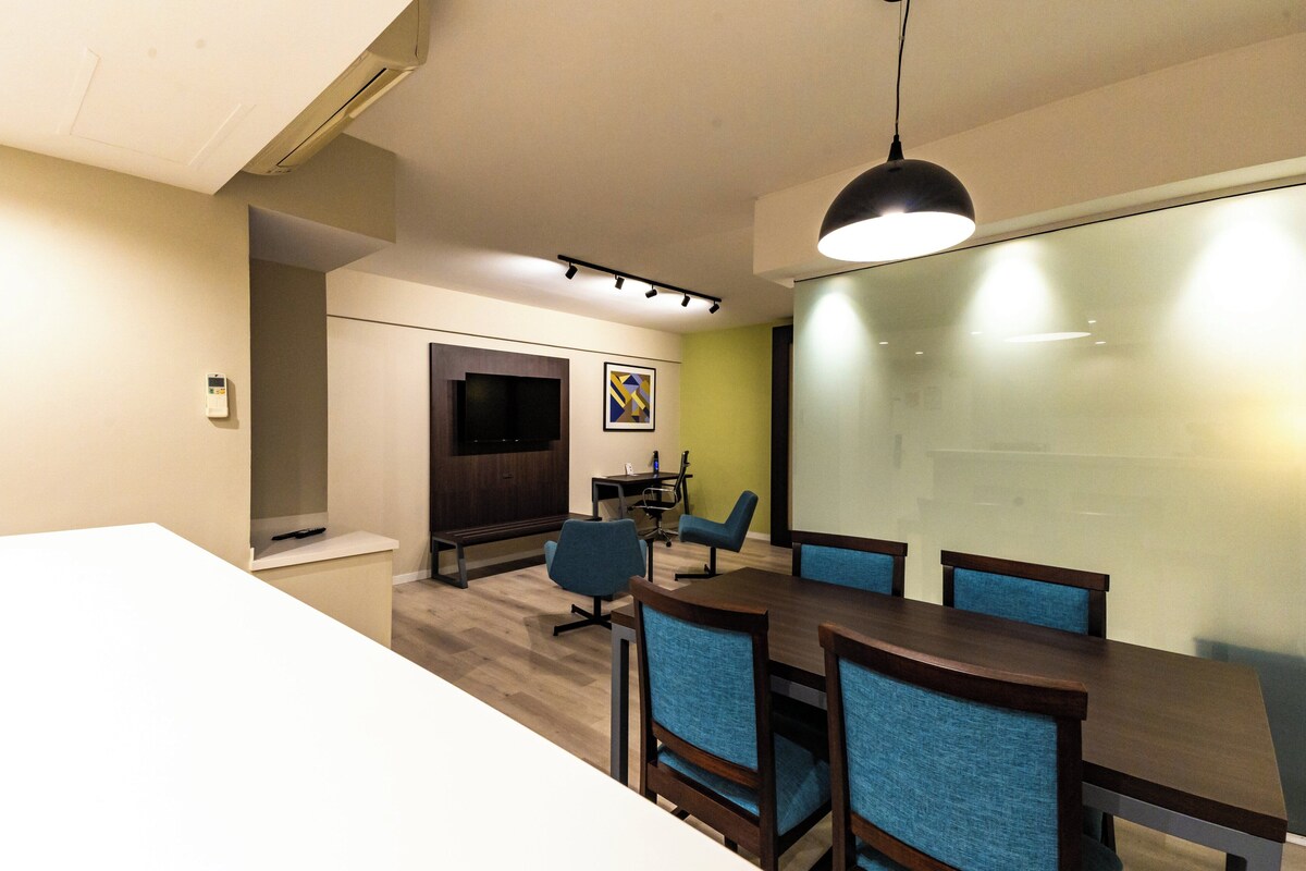 A conference room with a long table, blue chairs, a projector screen, and a whiteboard.