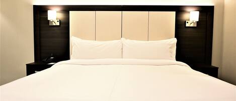 A hotel room with a large bed, two bedside tables, and wall-mounted lamps.