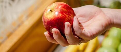 Una mano sosteniendo una manzana roja, con una variedad de frutas y verduras al fondo.