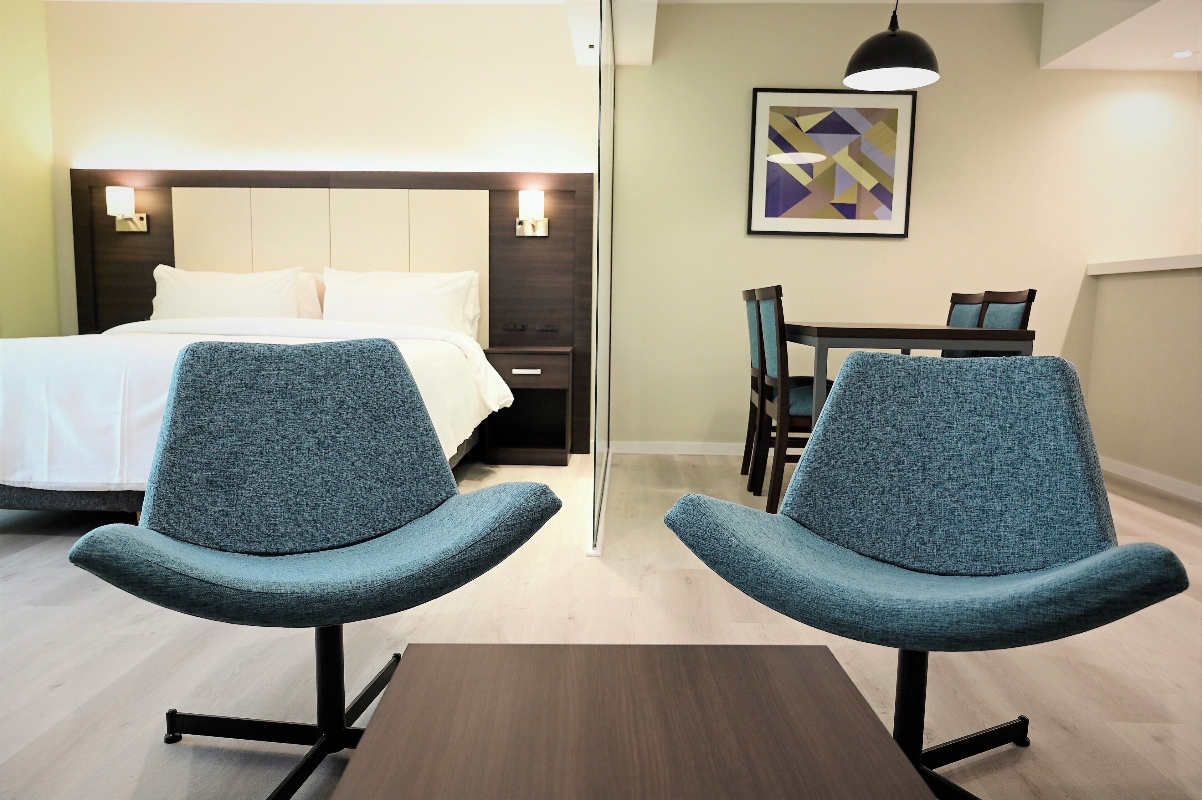 Ein Hotelzimmer mit einem Bett, zwei Stühlen, einem Tisch, einem Schreibtisch und einem Bild an der Wand.