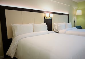 A hotel room with two beds, a headboard, a nightstand, and a lamp.