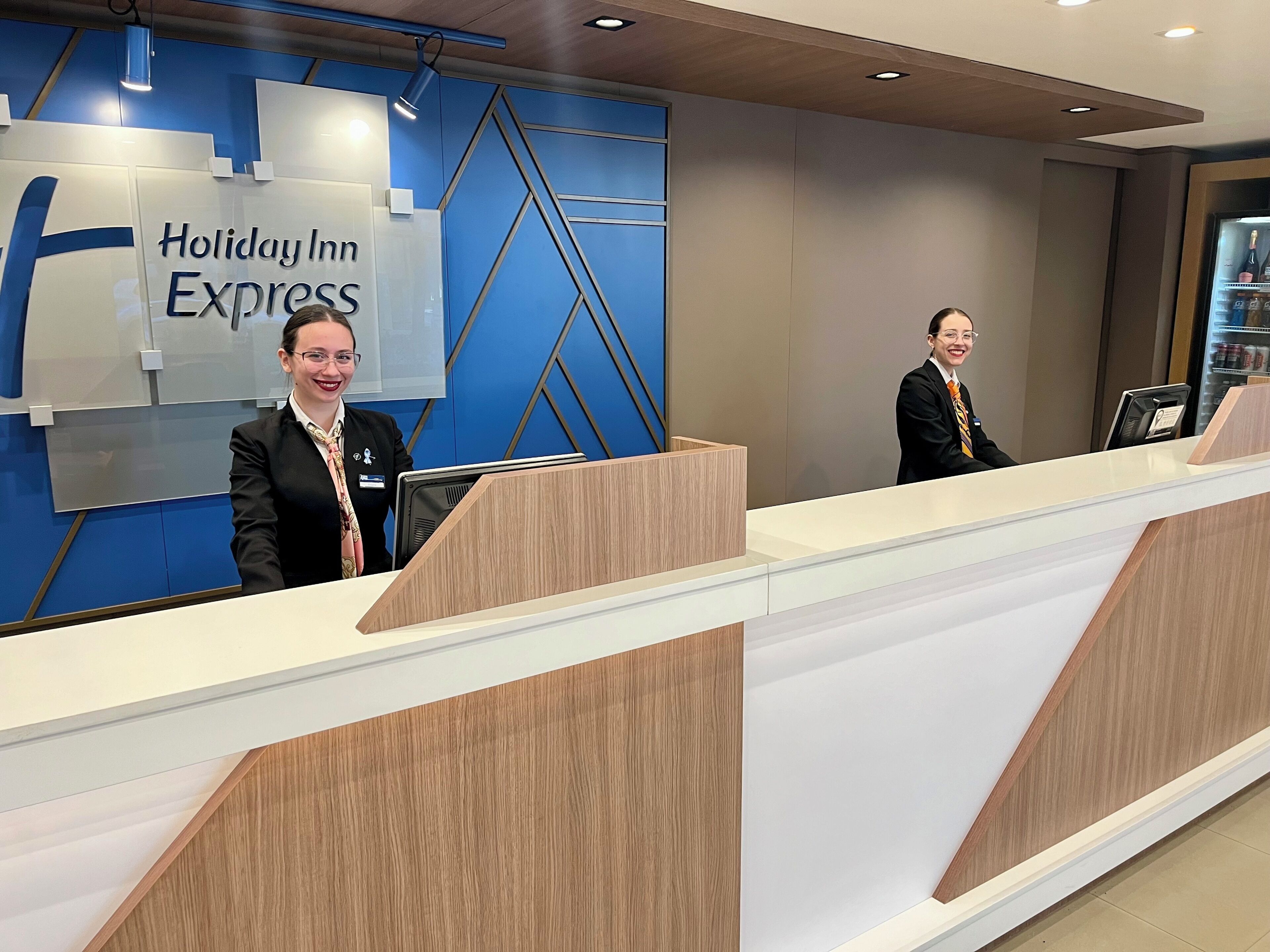 A Holiday Inn Express reception desk with two staff members, a blue wall with geometric patterns, and a modern design.