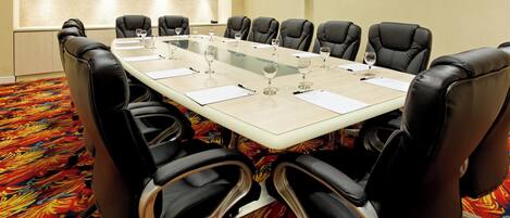 A conference room with a long table, black leather chairs, and a patterned carpet.