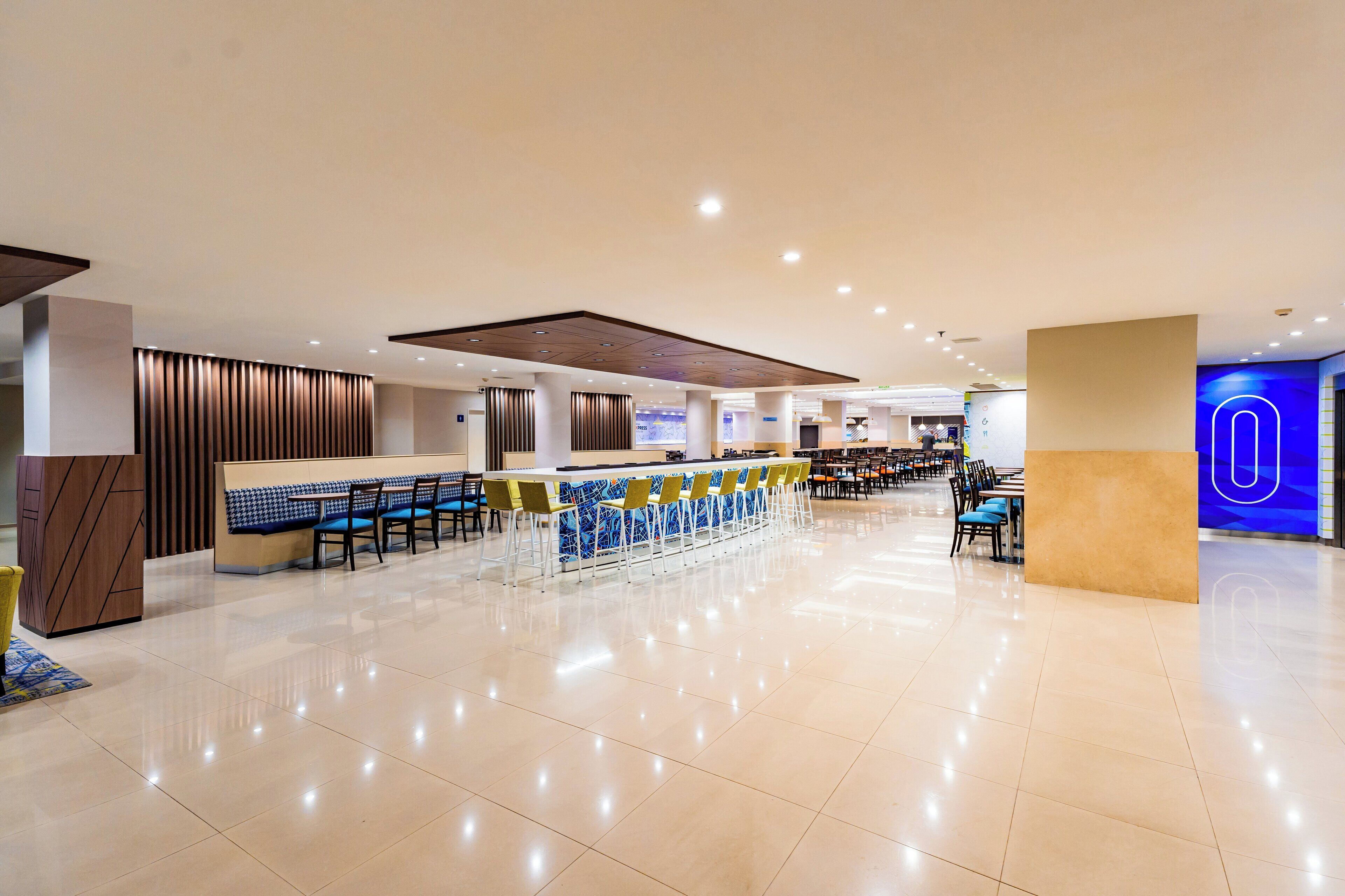 A spacious, modern hotel lobby with a long reception desk, multiple seating areas, and a clean, polished floor.