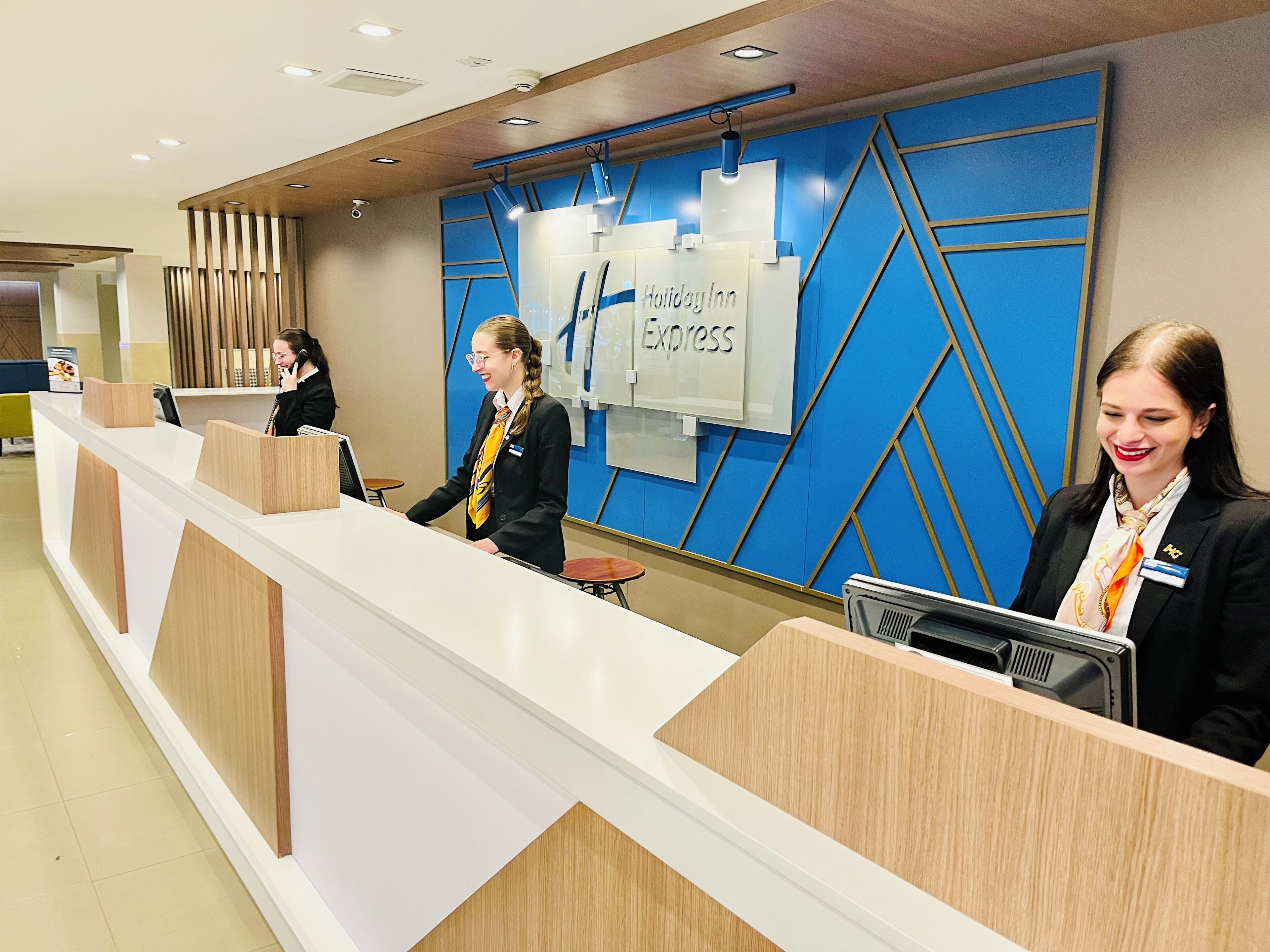A hotel reception desk with a blue geometric wall design and a sign reading "Holiday Inn Express".