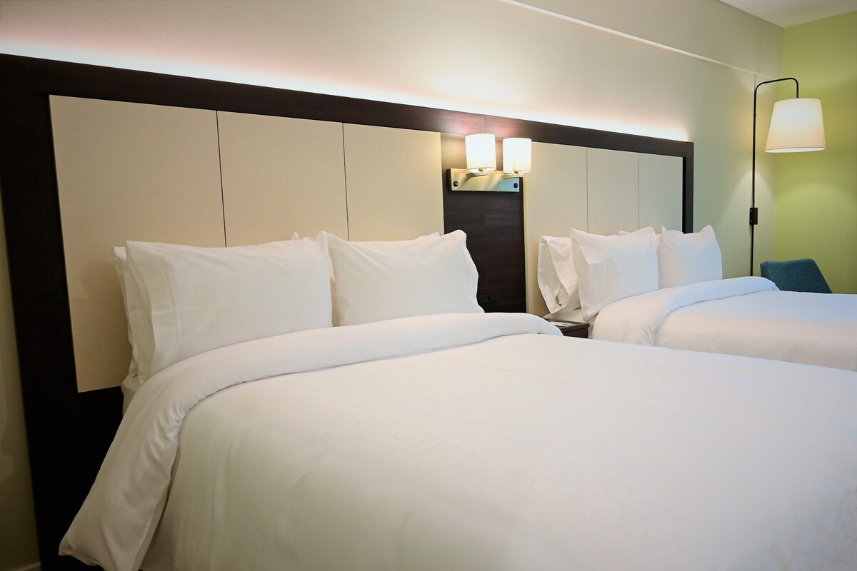 A hotel room with two beds, a headboard, a nightstand, and a lamp.