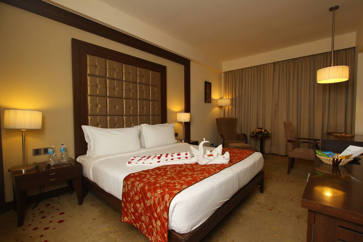 Ein Hotelzimmer mit einem großen Bett, zwei Nachttischen, einem Schreibtisch, einem Sessel und einer Lampe.