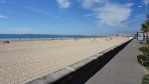 A wide sandy beach with a paved walkway on the right, leading to a cityscape in the distance. -  The Originals City, Hôtel Anaïade, Saint-Nazaire-Pornichet (Saint-Nazaire)