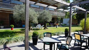 An outdoor patio area with wooden tables and chairs, surrounded by potted plants and a wooden pergola. -  The Originals City, Hôtel Anaïade, Saint-Nazaire-Pornichet (Saint-Nazaire)