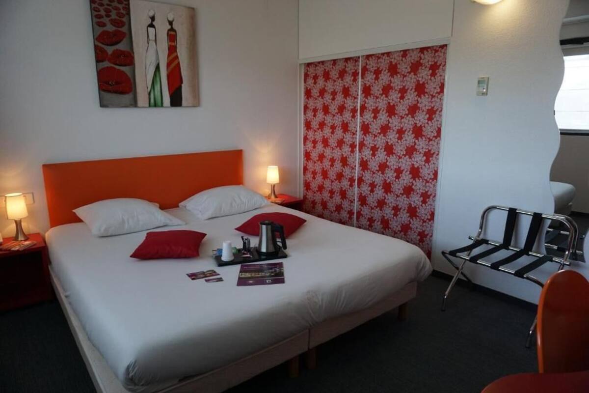 A hotel room with a large bed, two bedside tables with lamps, a red and white floral curtain, a black and white chair, and a red chair.