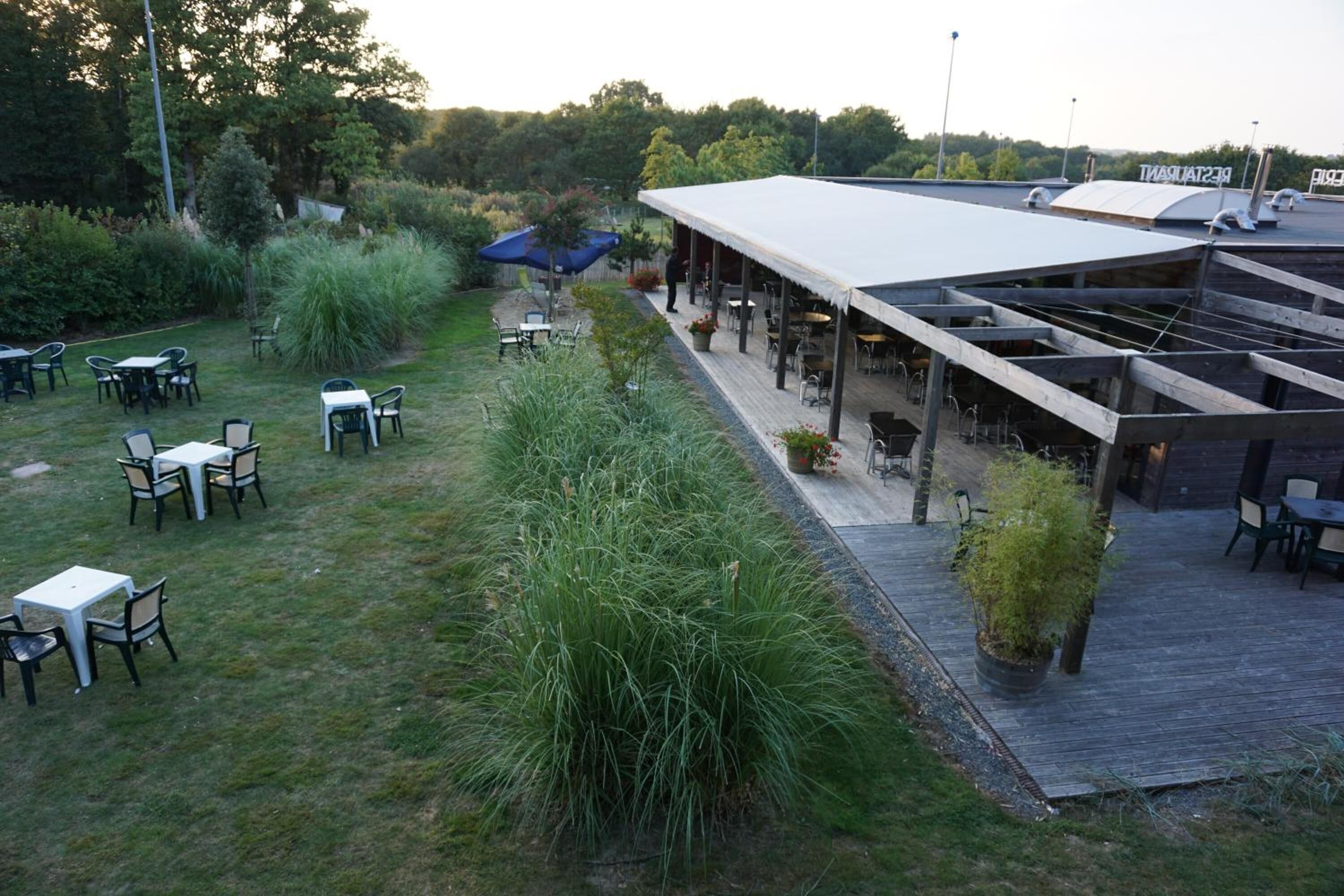 An outdoor patio area with tables and chairs, surrounded by greenery and a covered seating area.