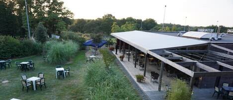 An outdoor patio area with tables and chairs, surrounded by greenery and a covered seating area.