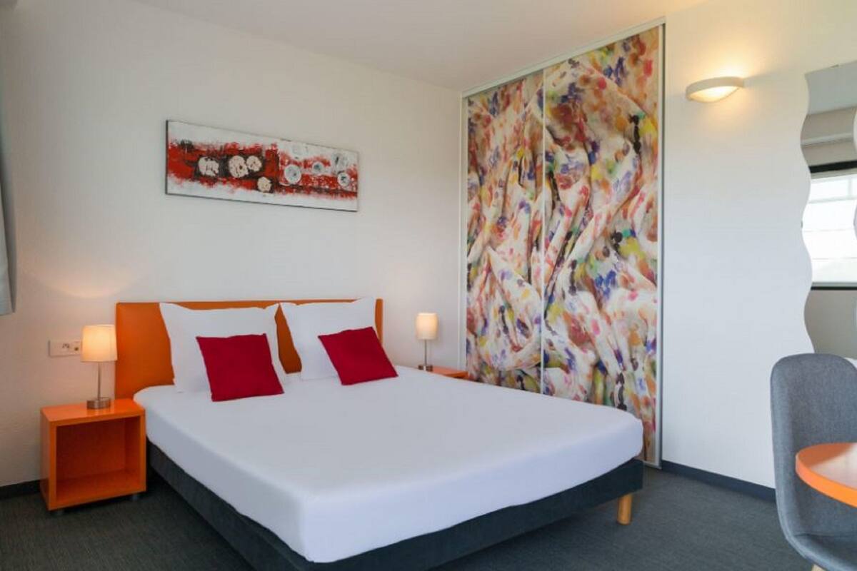 A hotel room with a large bed, two nightstands, a chair, and a colorful abstract painting on the wall.