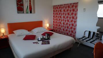 Ein Hotelzimmer mit einem großen Bett, zwei Nachttischen mit Lampen, einer roten und weißen floralen Trennwand, einem schwarz-weißen Stuhl und einem roten Stuhl.