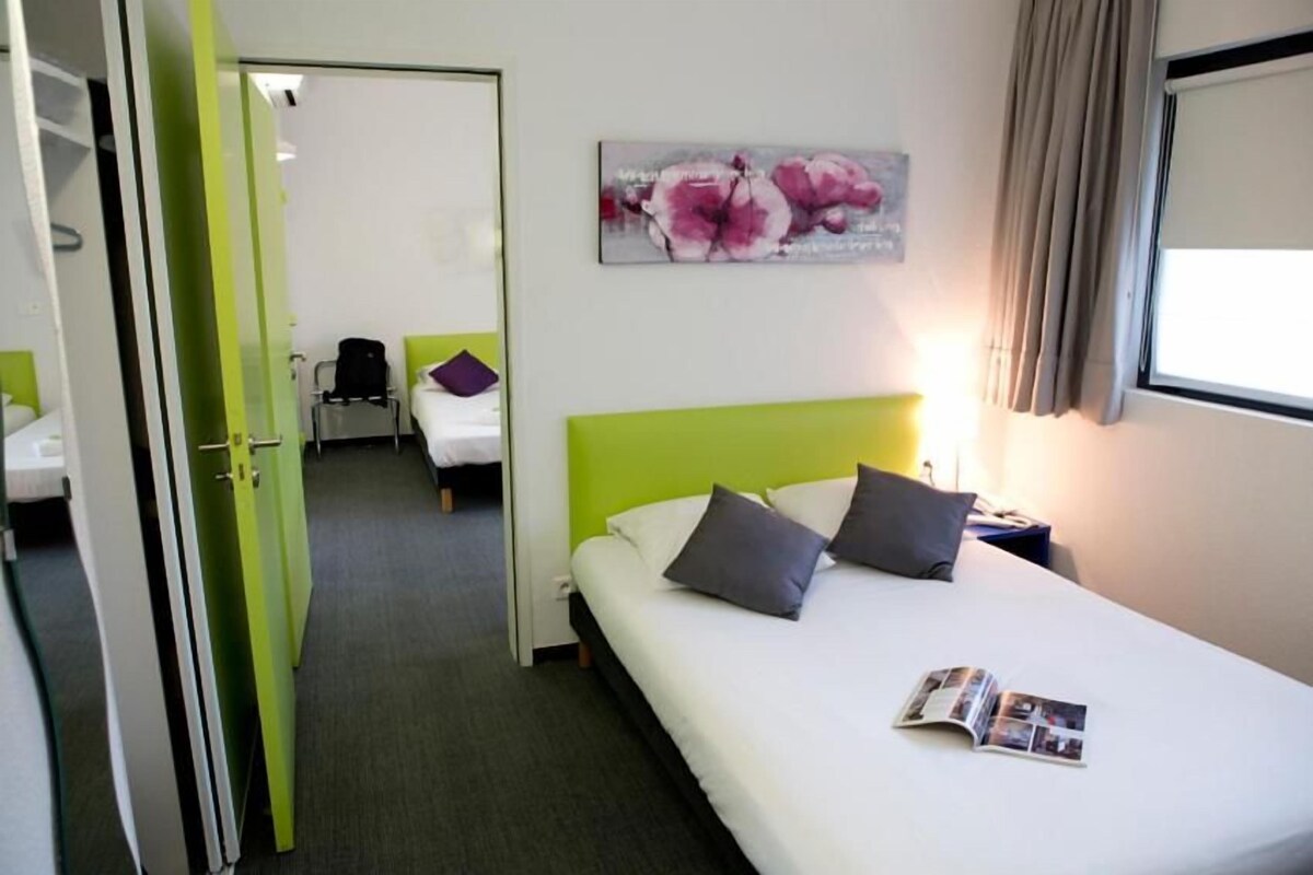 Una habitación de hotel con una pared verde decorativa, una cama con dos almohadas, una mesita de noche con una lámpara y un cuadro de flores en la pared.