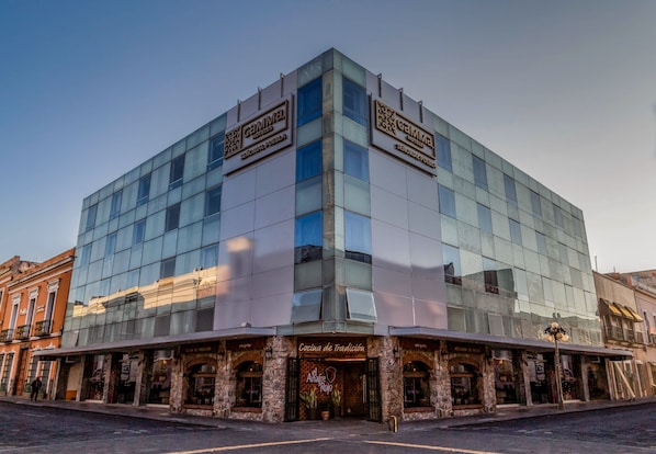 A modern hotel with a glass facade, a traditional facade entrance, and a sign for 'Cocina de Tradición'.