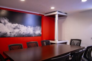 Uma sala de conferências com uma mesa comprida, seis cadeiras e um quadro abstrato grande na parede.