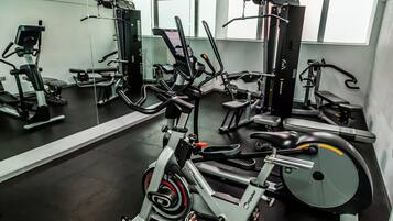 A gym with various exercise equipment, including a stationary bike, weight machines, and a bench.