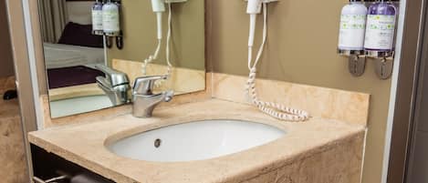 A bathroom with a beige marble sink, a mirror, a towel rack, and a hairdryer on the wall.