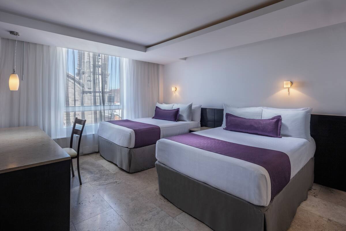 A hotel room with two beds, a desk, and a chair.