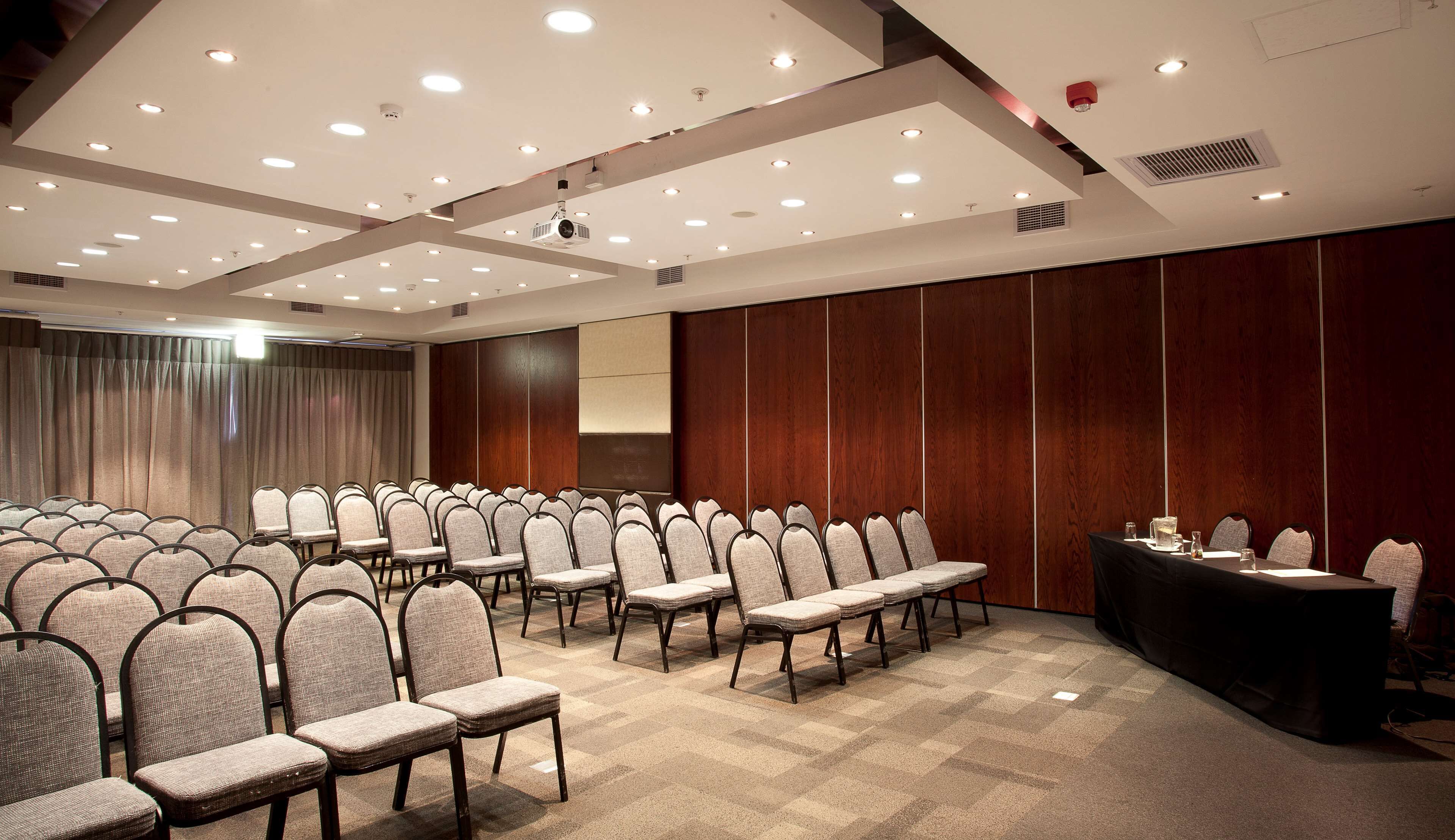 A conference room with rows of chairs, a long table, and a projector screen.