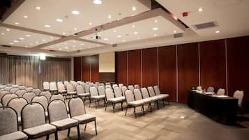 A conference room with rows of chairs, a long table, and a projector screen.