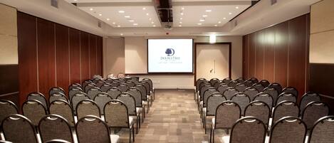 A conference room with rows of chairs facing a projection screen displaying a logo.