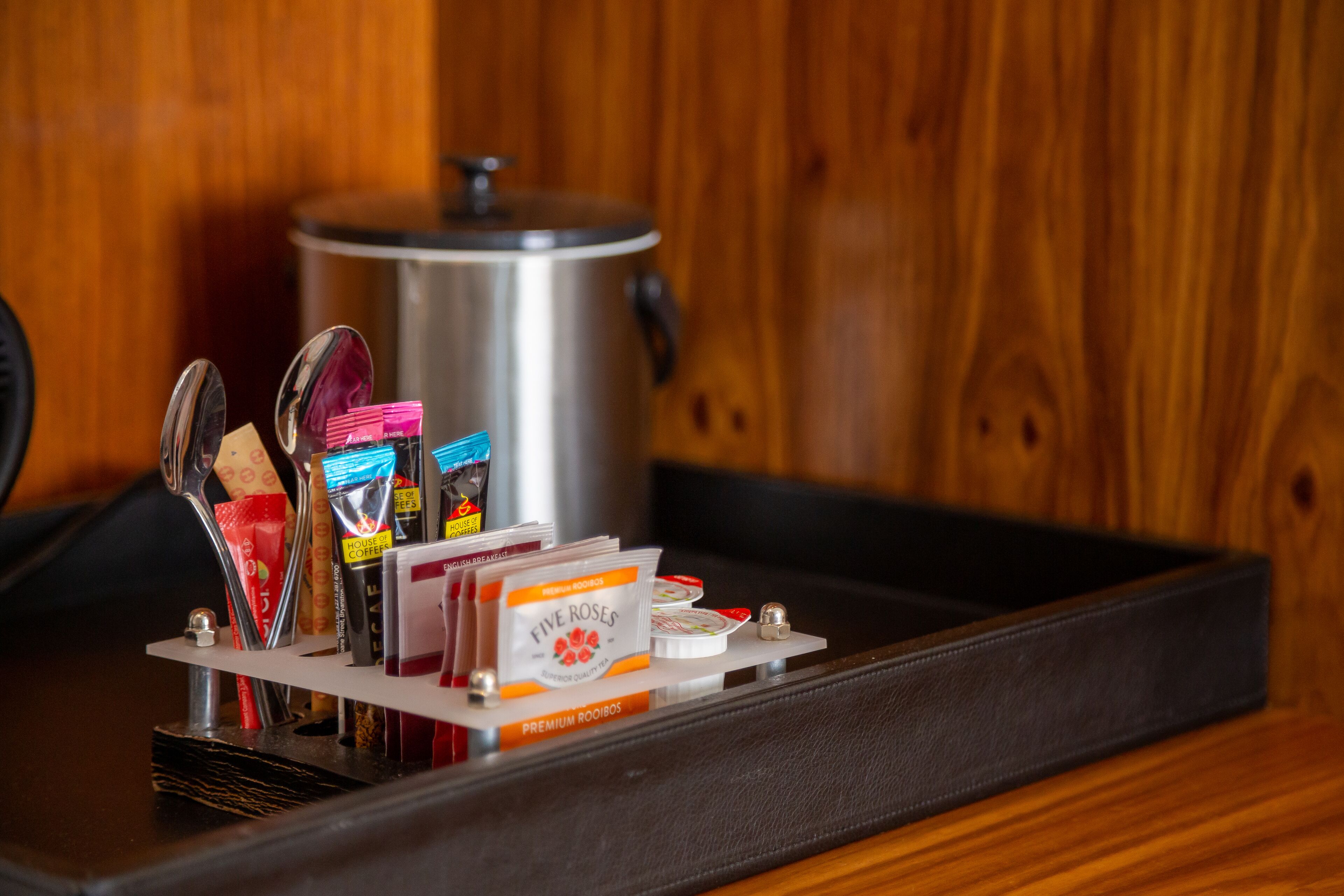 A tray with coffee and tea packets, a spoon, and a teapot on a wooden surface.