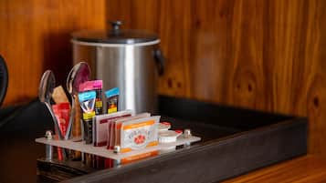 A tray with coffee and tea packets, a spoon, and a teapot on a wooden surface.