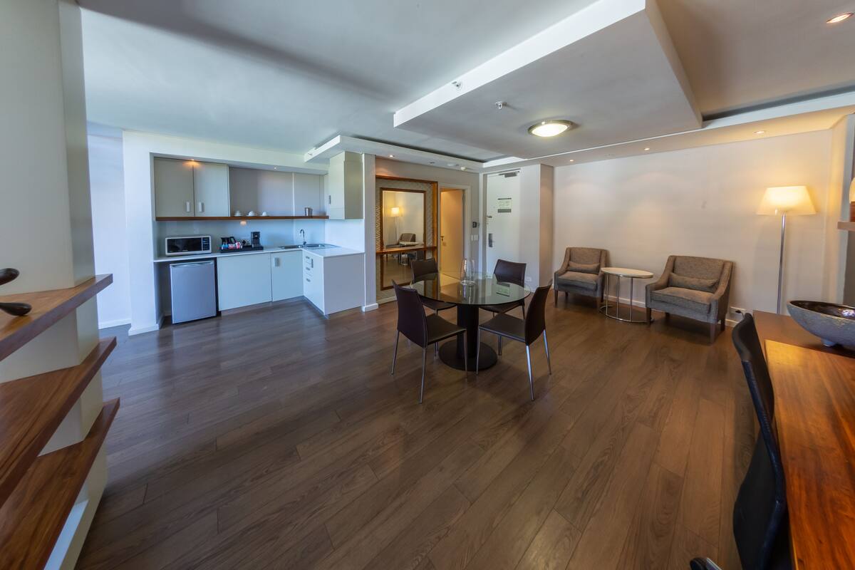 Een moderne hotelkamer met een zithoek, kitchenette en een eethoek met een lamp.