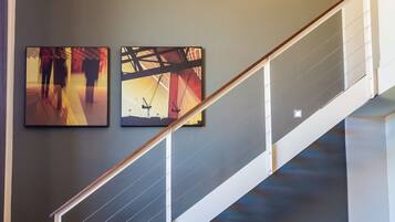 A modern interior with a staircase, two wall-mounted artworks, and a sofa with cushions.