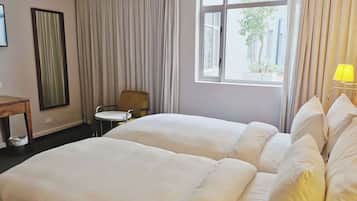 Une chambre d’hôtel avec deux lits, une chaise, une table, un miroir et une fenêtre avec des rideaux.