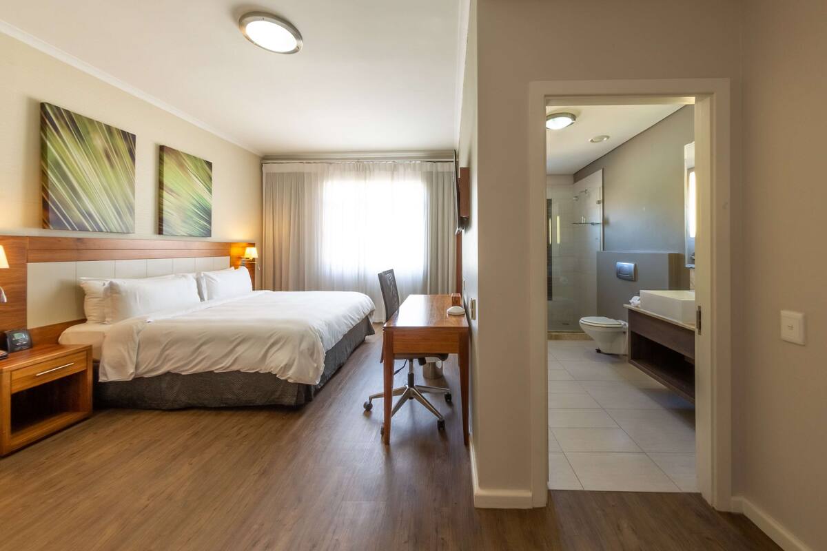Een hotelkamer met een bed, nachtkastje, bureau, stoel en uitzicht op de badkamer.