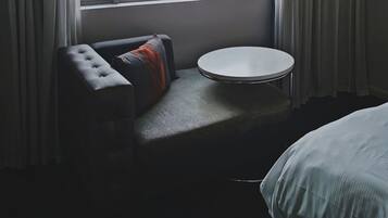 A hotel room with a large window, a sofa, a small round table, and a bed.