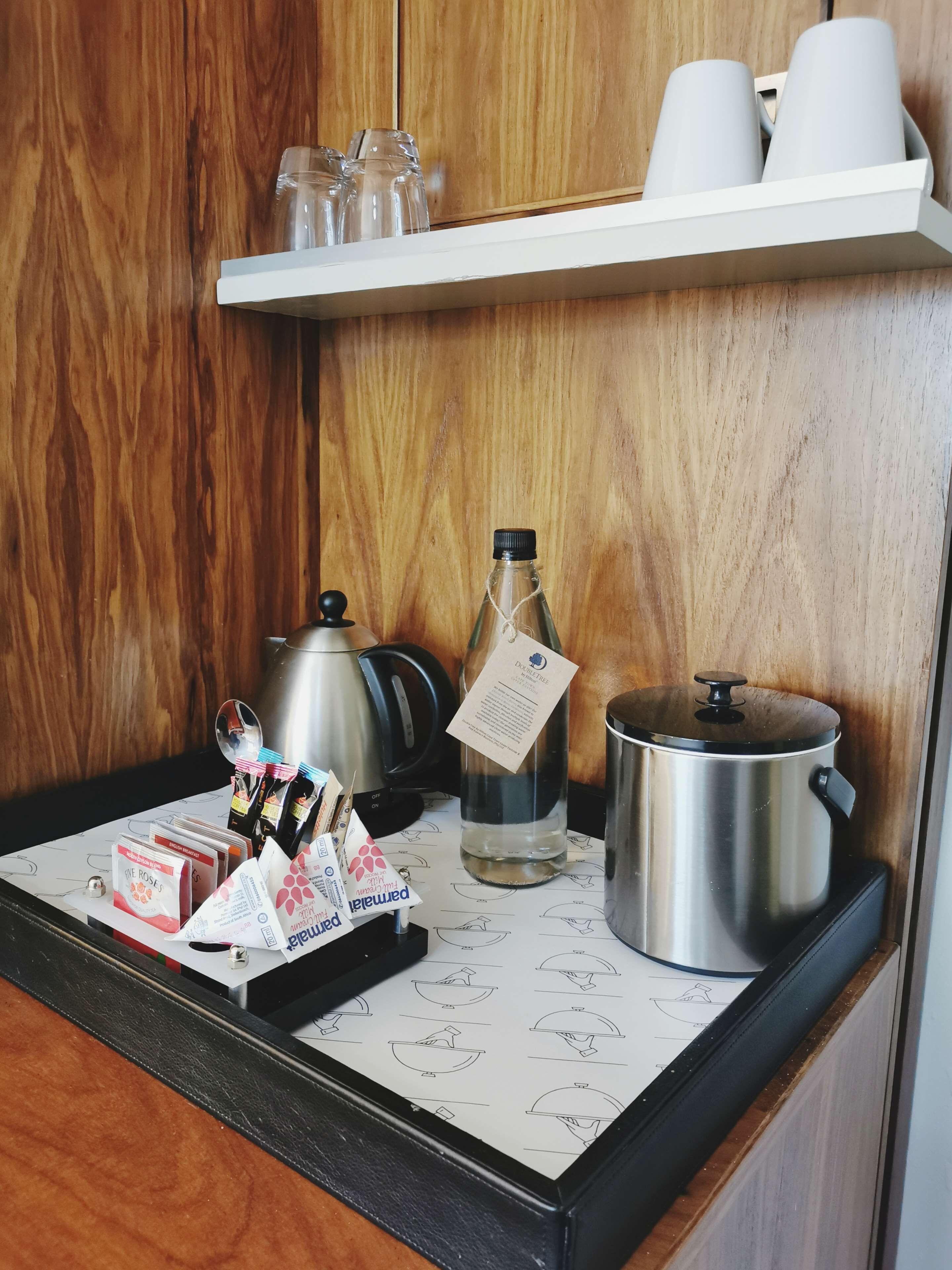 A kitchen counter with a coffee maker, a kettle, a bottle of water, and a pot on a stove.